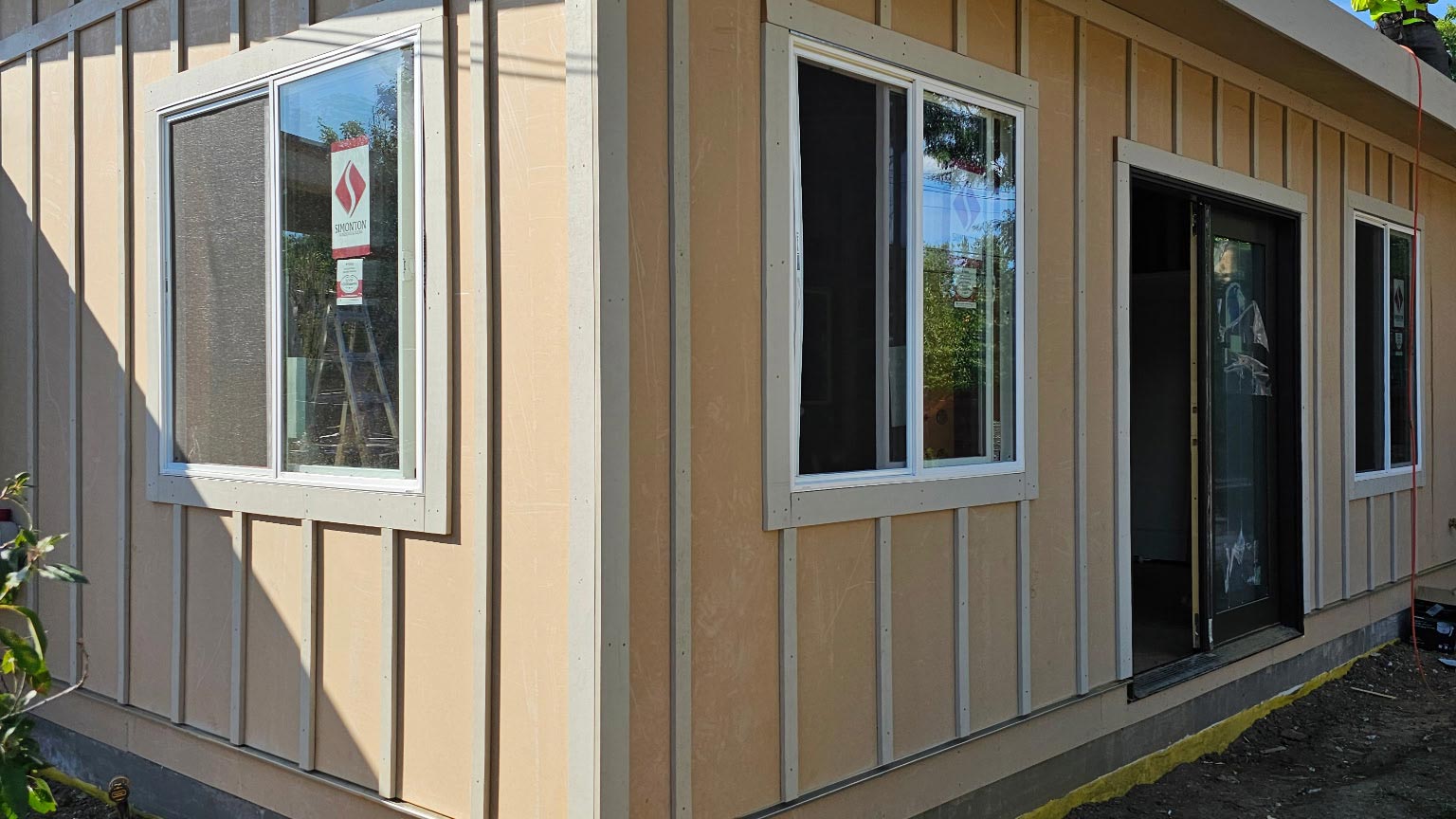 Modern home addition with tan board-and-batten siding and a flat roof, built by BH Builders