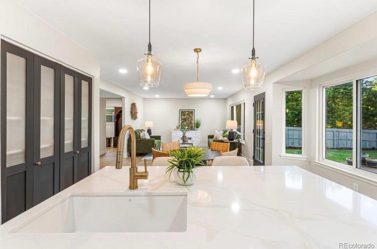 Marble waterfall kitchen island with gold faucet opening to a large living area in a BH Builders renovation