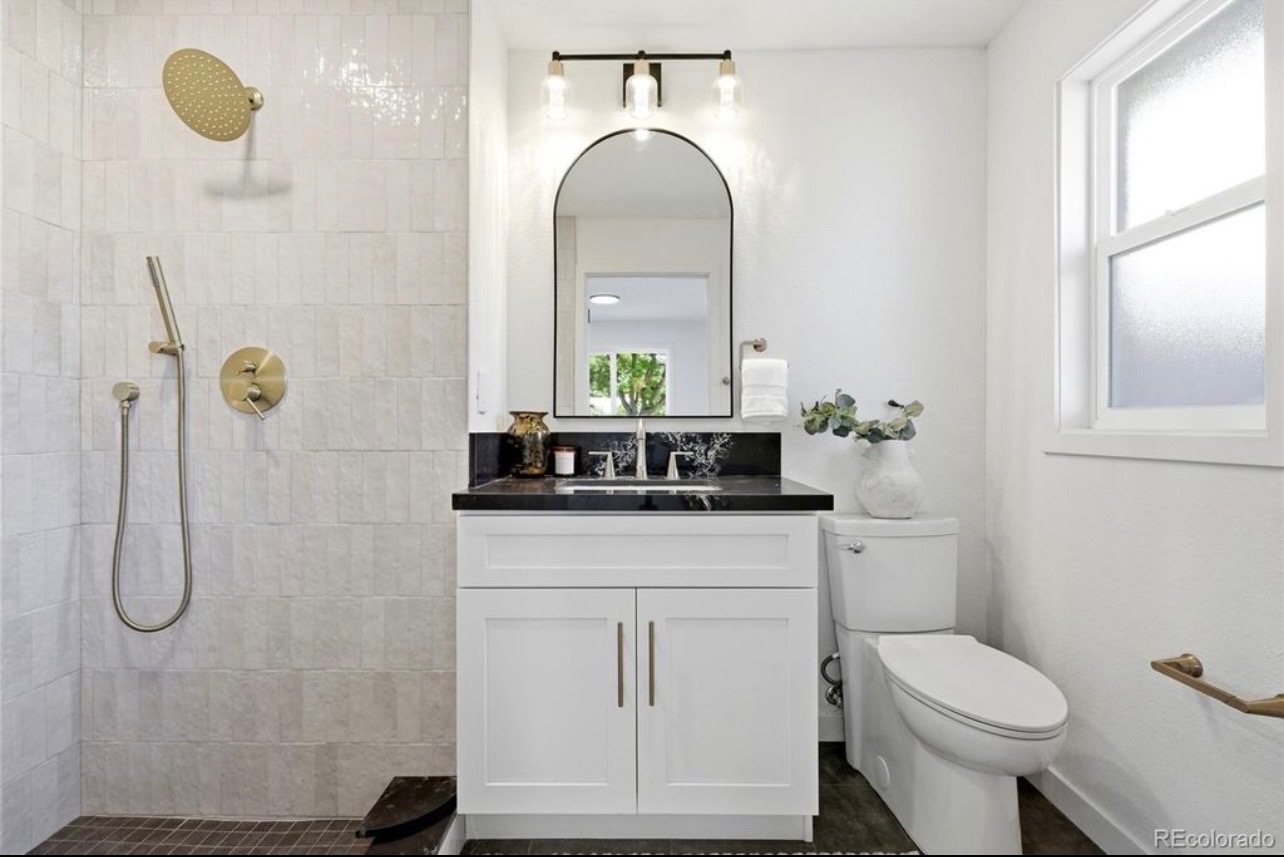 Completed walk-in shower with white zellige tile, brushed-gold fixtures and adjacent white vanity with dark counter