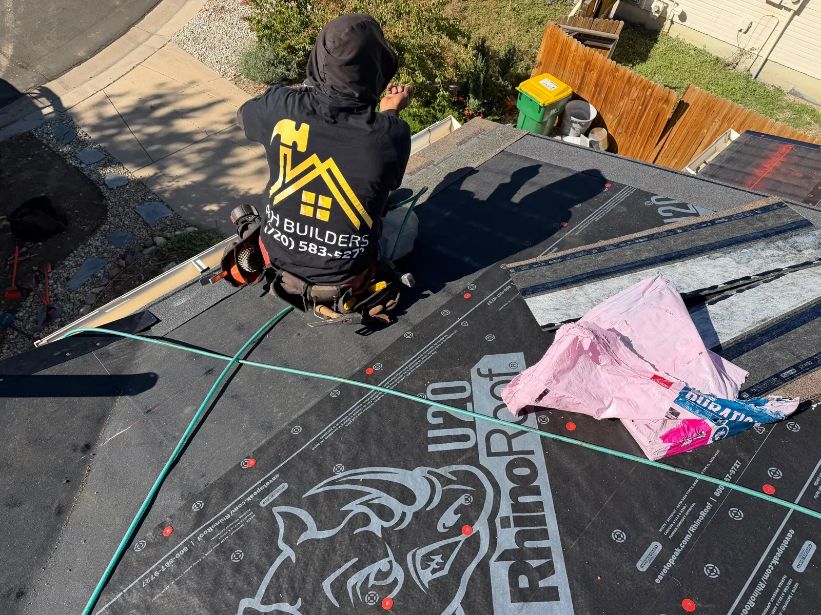 Black RhinoRoof underlayment covers the roof slope below a kneeling worker, with an air hose crossing the surface.