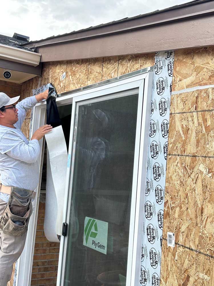 Craftsperson installing flashing tape around a residential window while the exterior weather barrier remains exposed