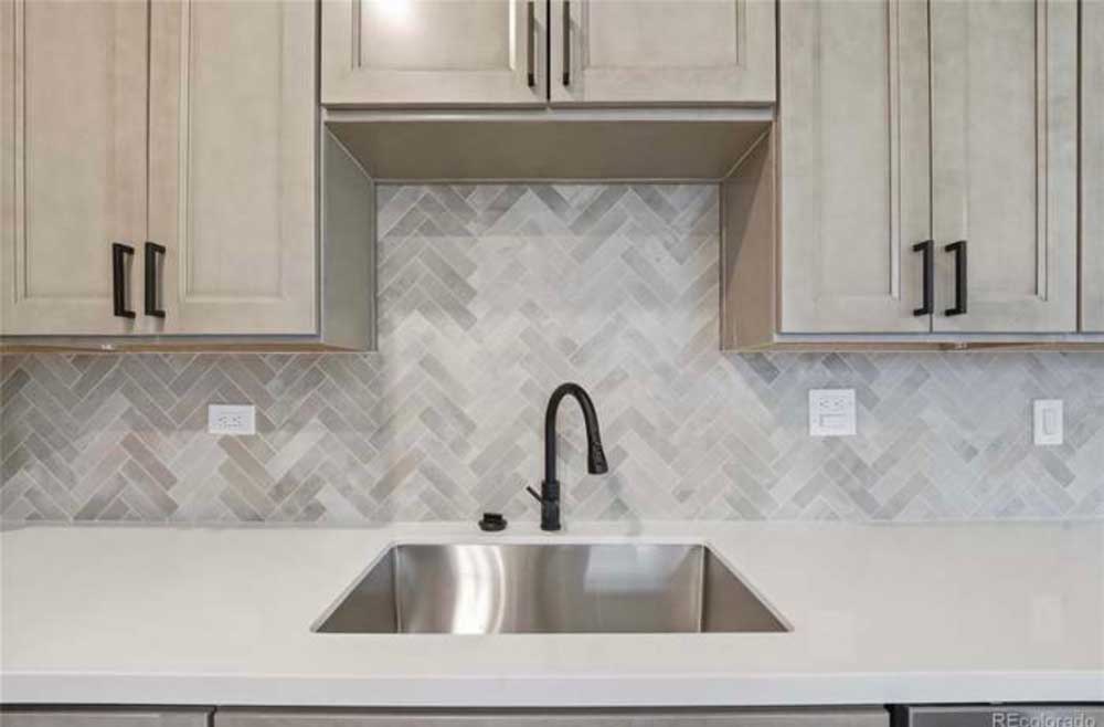 Close-up of a quartz countertop and white herringbone tile backsplash at the kitchen sink