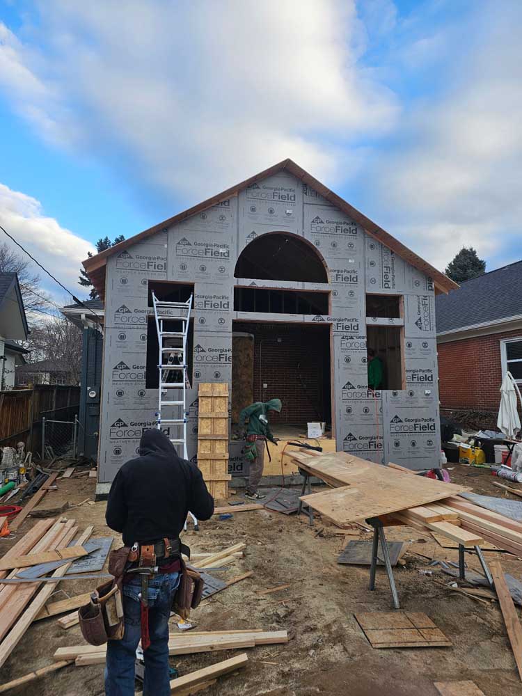 Rear residential addition with wall sheathing and roof tie-in visible before weather barrier and exterior finishes