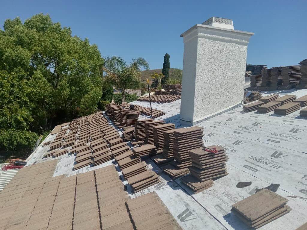 Concrete roof tiles stacked on high-temp underlayment around a stucco chimney during a re-roof