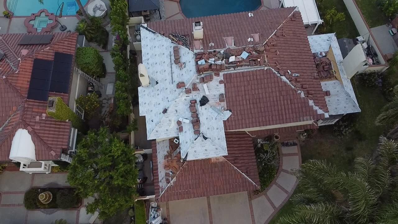 Aerial of an estate home tile roof replacement with underlayment sections and staged tile bundles