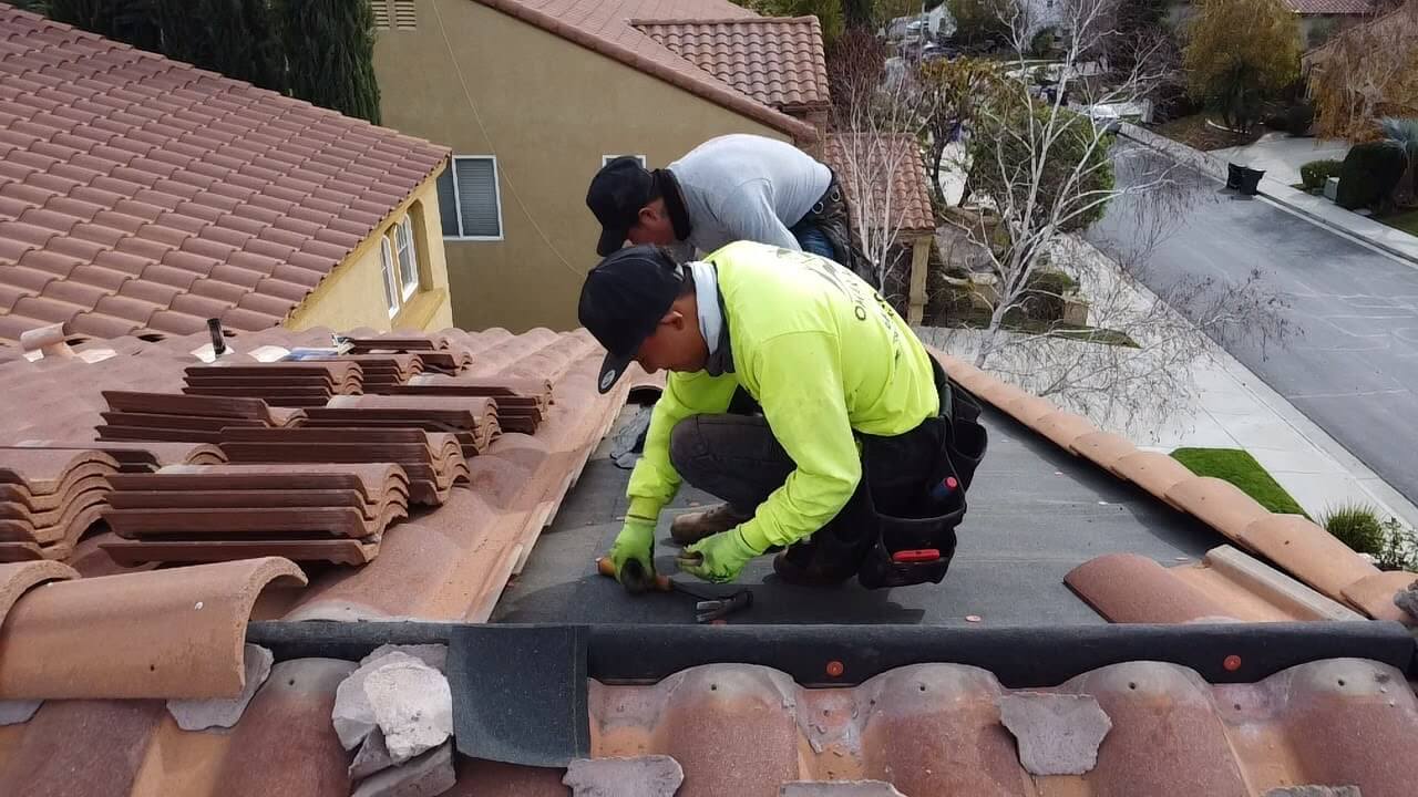 Two roofers installing underlayment and battens on a concrete tile roof