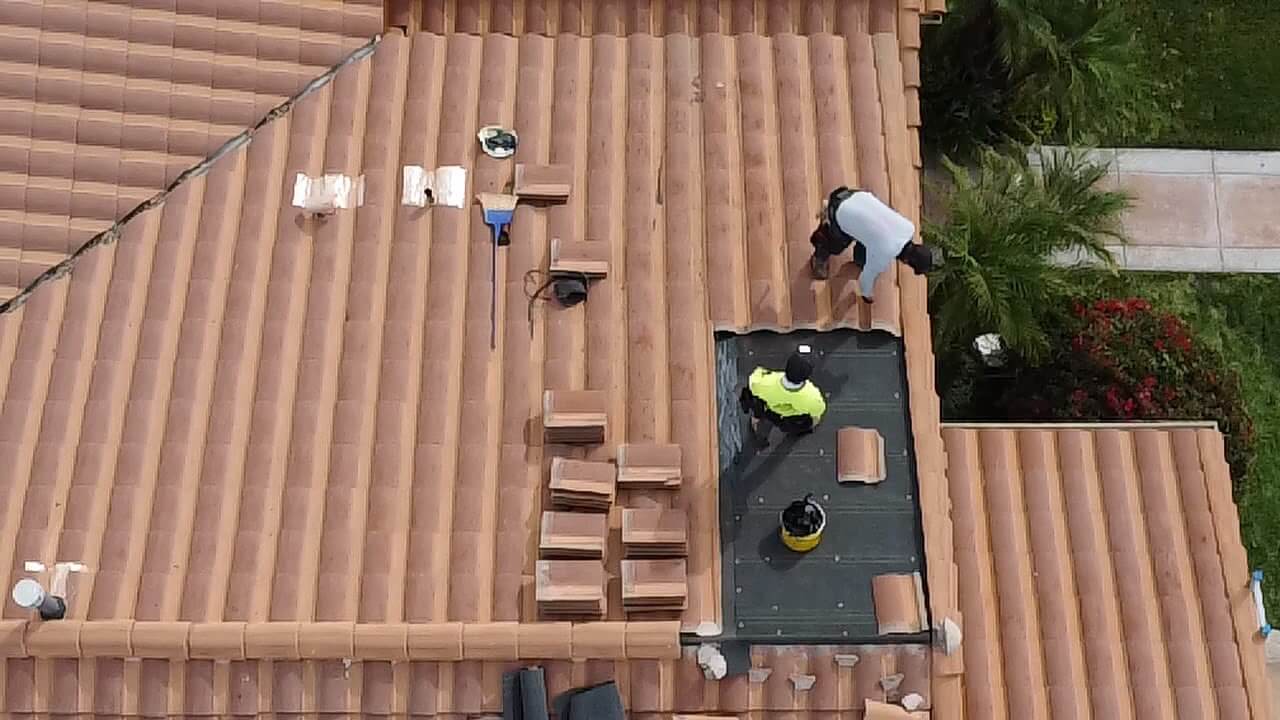 Roofing crew repairing a tile roof section with membrane underlayment exposed