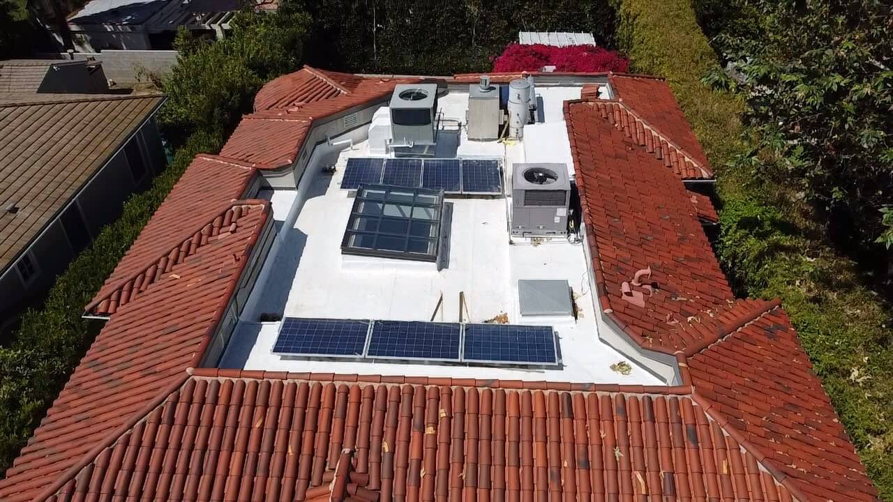 Aerial of a Spanish tile roof with a white flat membrane center, solar panels and a large skylight